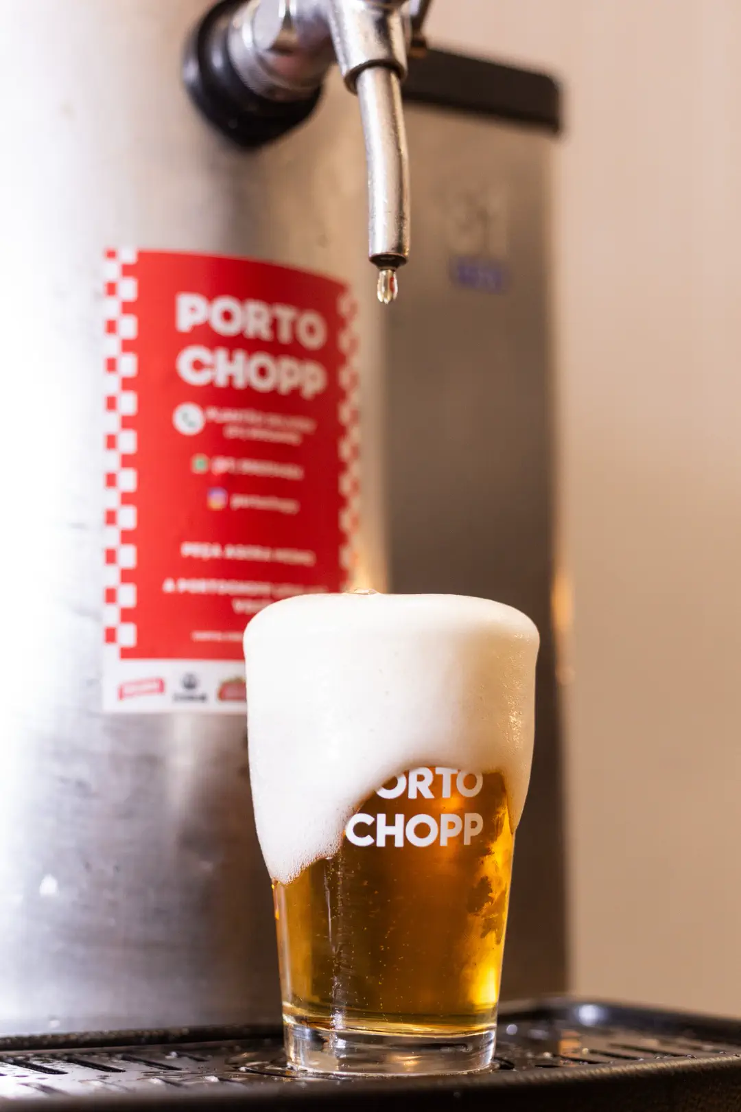Copo de chopp transbordando espuma, com a marca Porto Chopp impressa, servido na chopeira